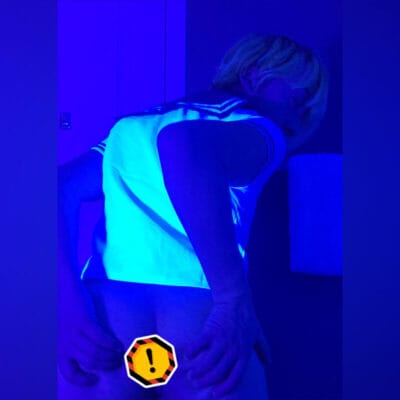Person in a sailor-style shirt shown from behind, bending over in a blue-lit room; a yellow warning badge covers part of the lower back/buttocks area.